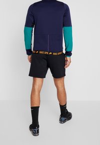 Abbigliamento sportivo Nike con una parte superiore blu navy, maniche teal e pantaloni neri. Presenta il logo sulla vita e maglie lavorate a trama.