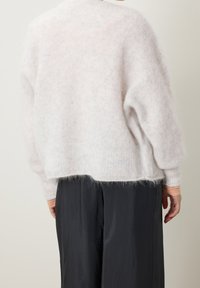 Vaaleanpunainen pörröinen neulepaita, jossa on rento istuvuus, pyöreä kaula-aukko ja ribattu helma. Pitkät, löysät hihat, joissa on pehmeä, teksturoitu pinta.