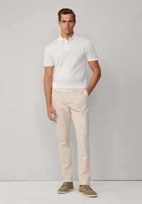 Polo shirt bianco a maniche corte, pantaloni beige e scarpe casual grigie. Il polo presenta un colletto e un logo discreto sul petto.