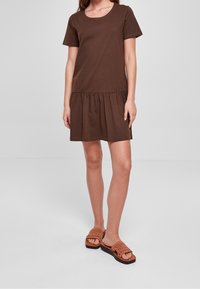 Hnědressová bavlněná šaty s krátkými rukávy a volánkovým lemem, doplněné hnědými tkanými pantofli na plošině.