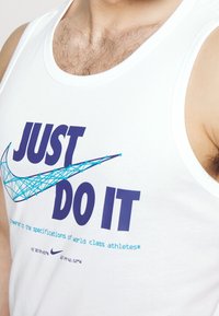 Witte tanktop met grote blauwe tekst "JUST DO IT" en een blauwe geometrische Nike swoosh op de borst en schouder van een persoon.