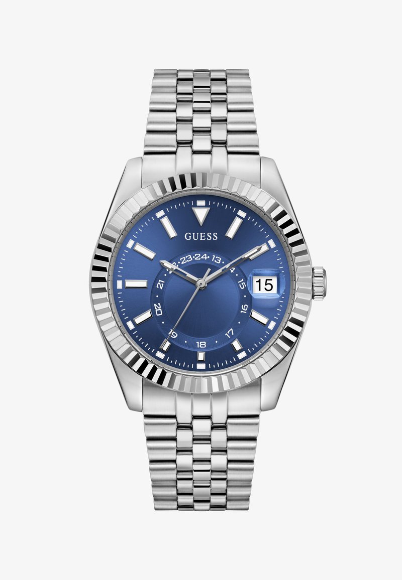 Silver metal bracelet watch with blue dial, white hour markers, date window showing 15, and brand name "GUESS" below 12 o'clock.