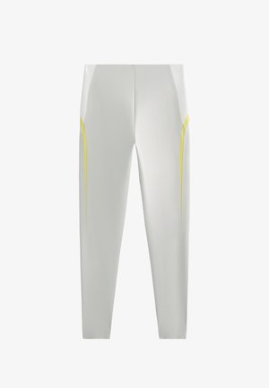 Leggings atletici bianchi presentano un design snello con accenti gialli sui lati. Realizzati in un tessuto liscio ed elastico, hanno una silhouette aderente.