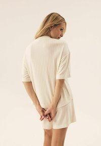 Cream-colored loungewear set made of ribbed fabric, featuring a loose-fitting short-sleeve top and matching shorts.