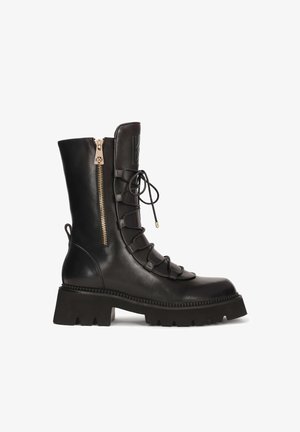Bottes noires en cuir, hauteur jusqu'au genou, avec un cordon à l'avant, une fermeture éclair sur le côté, une semelle texturée épaisse et un détail de logo sur la tige. Présente des accents en matériel doré.