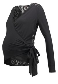 Blouse cache-cœur noire à manches longues avec panneaux en dentelle florale sur les épaules et les côtés, nouée en nœud sur le côté à la taille.