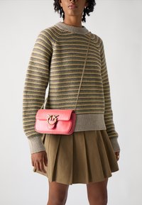 Small pink leather crossbody bag with a metal clasp, paired with a striped sweater and a pleated olive skirt. Textured details visible.