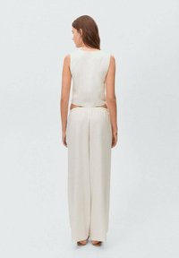 Svijetlo bež skratni top i široke hlače, izrađeni od mekanog materijala. Imaju glatku teksturu i minimalistički dizajn.