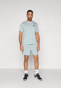 Αθλητική μπλούζα και σορτς σε ανοιχτό γαλάζιο χρώμα, κατασκευασμένα από αναπνεύσιμο ύφασμα. Διακοσμημένα με μαύρες λογότυπες λεπτομέρειες. Συνδυάζονται με μαύρα αθλητικά παπούτσια και λευκές κάλτσες.