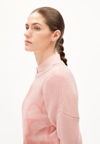 Weicher rosa Pullover mit strukturiertem Strick und floralem Muster, kombiniert mit einem hellrosa Hemd mit Kragen. Schlichtes, modernes Design.