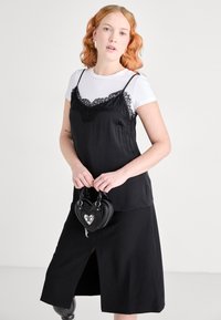 Musta satiini liukuva mekko, jossa on pitsireunus, kerroksittain valkoisen T-paidan päällä. Malli pitää pientä mustaa sydämenmuotoista laukkuja. Sileä pinta ja yhtenäiset värit.