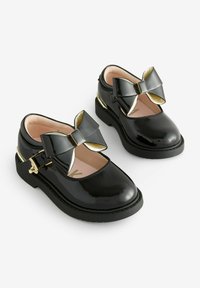 Scarpe Mary Jane in vernice nera con un brillante fiocco nero e accenti dorati. Presentano una punta arrotondata e un interno imbottito.