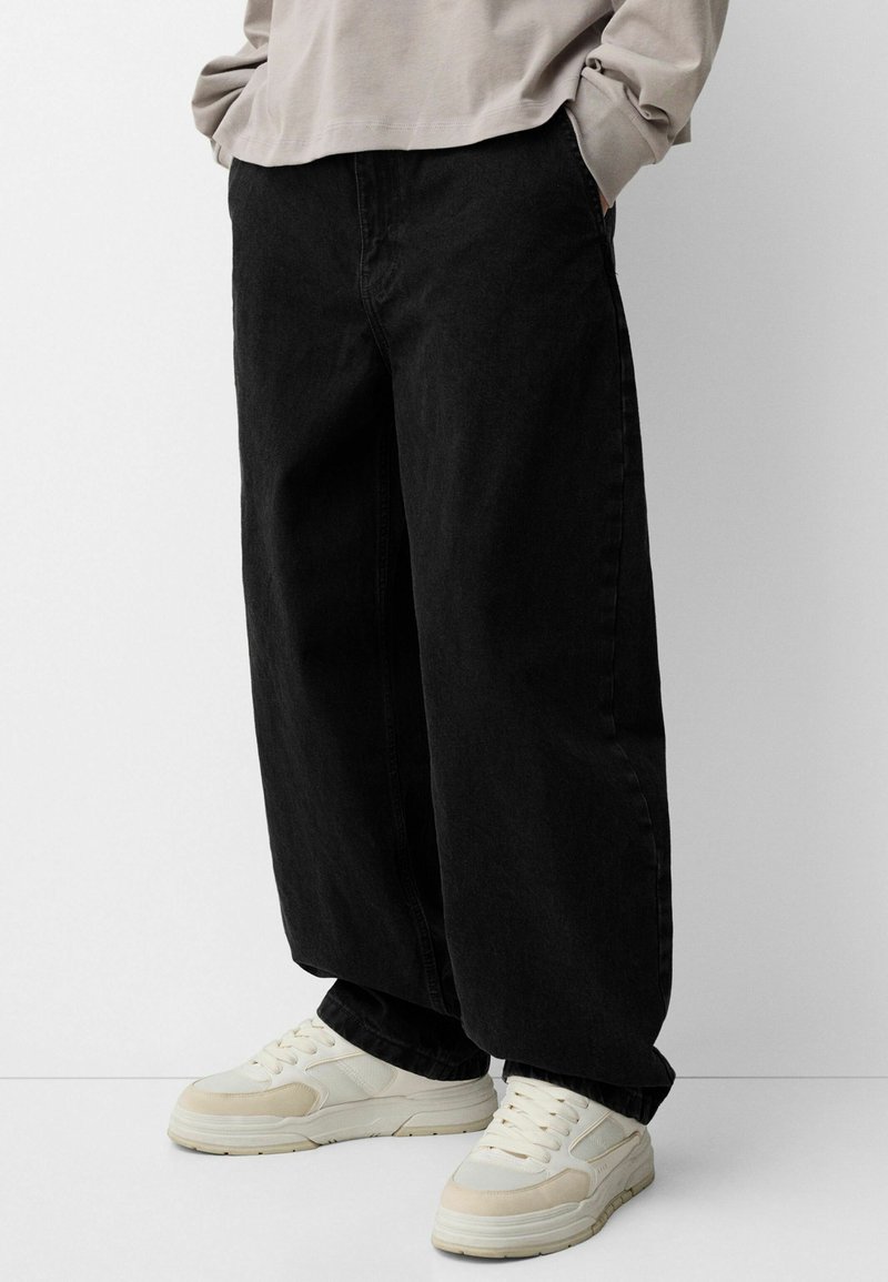 Black wide-leg denim jeans with a slightly faded texture, paired with cream sneakers featuring light accents and a chunky sole.