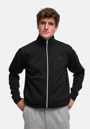 Black zip-up jacket with a high collar and white zipper, made of soft fabric, featuring long sleeves and a subtle logo on the chest.