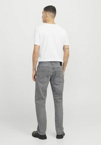 Jean en denim gris à coupe droite, avec des poches arrière brodées et une étiquette noire, accompagnés d'un t-shirt blanc unis et de chaussures noires.