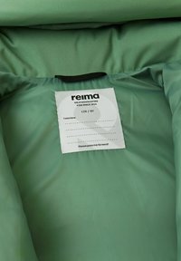 Zielona lekka kurtka wewnątrz z miękkiego materiału. Metka mówi "reima", wskazuje rozmiar 128/8Y oraz zawiera instrukcje dotyczące pielęgnacji i dedykację.