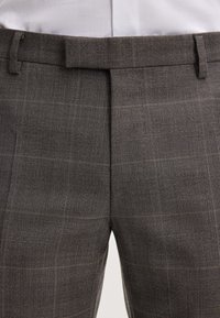 Grijze gemusterde broek met een gestructureerde stof, vlakke voorkant en subtiele bruine accentlijnen. Voorzien van een ceintuurlussen en een getailleerde pasvorm.