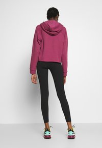 Sudadera de felpa en rosa oscuro con textura acanalada, diseño corto y capucha. Combinada con leggings negros y zapatillas multicolores.