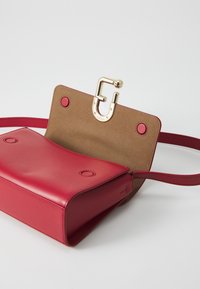 Borsa a tracolla in pelle rossa con esterno liscio, interno in suede color beige e chiusura in metallo dorato; include una lunga tracolla e dettagli circolari.
