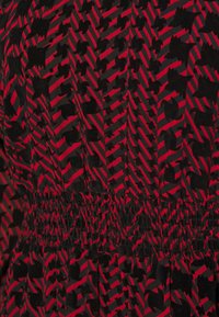 Röd och svart mönstrad tyg med vertikala ränder och abstrakta former. Rynkad midja som ger textur. Slätt, lätt material.