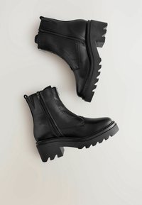 Black leather ankle boots with a chunky textured sole, dual side zippers, and a seam detail on the upper for added durability.