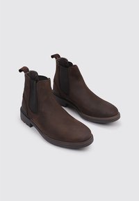 Bottines en cuir marron avec des panneaux élastiques sur les côtés, bout rond et semelle en caoutchouc robuste. Texture lisse avec des détails de couture contrastants.