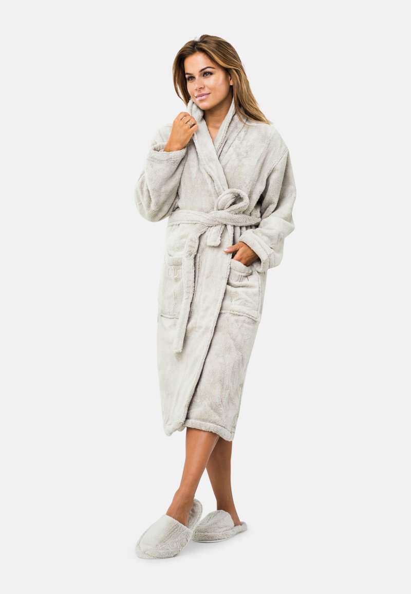 Šviesiai pilkas, paminkštintas vonios chalatas su šaliku ir dviem priekinėmis kišenėmis; minkšta tekstūra; atitinkantys pūkuoti šlepetės užbaigia įvaizdį.