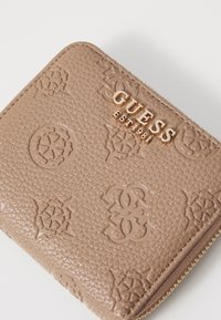 Smeđi teksturirani novčanik od umjetne kože s reljefnim uzorcima, zlatnim logotipom "GUESS EST. 1981" i zatvaranjem na zatvarač sa zlatnim priborom.