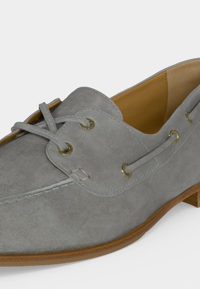 Γκρι μοκασίνι από σουέτ με γαζιά moc toe, δερμάτινα κορδόνια περασμένα από μπρούτζινα μεταλλικά ροζέτα και καφέ λαστιχένια σόλα.