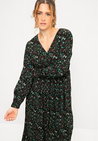 Vestido negro con un patrón abstracto colorido que presenta verde, rojo y blanco. Tiene mangas largas y un escote en V, con una falda fluida.