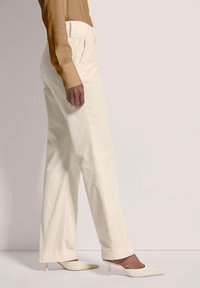 Crèmekleurige, gestreepte broek met een hoge taille, zijzakken en een rechte broekspijp, gecombineerd met puntige, witte hakken.