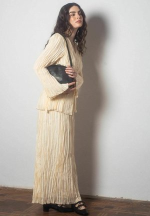 Abito plissettato avorio con maniche lunghe, una silhouette fluida, abbinato a una borsa nera texture e a delle scarpe ballerine nere con fiocchi.