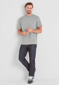 Gray short-sleeve t-shirt with a round neckline, paired with dark jeans and blue sneakers, standing against a white background.
