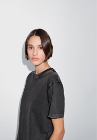 T-shirt nera, oversize, con collo tondo e maniche corte, caratterizzata da una texture sbiadita e dettagli con orlo grezzo, indossata su uno sfondo chiaro.