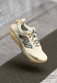 Kevyt juoksukenkä, väriltään off-white, jossa siniset yksityiskohdat, teksturoitu päällinen, pehmustettu kaulus ja kumipohja, joka on suunniteltu tarjoamaan pitoa ja kestävyyttä.