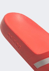 Rode schuimsandalen met textuurmateriaal, gevormde voetbed en een zilveren accentstreep. "adidas" is in de zijkant gedrukt.