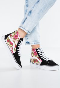 Baskets montantes en suède noir, avec des panneaux en tissu floral rose, des lacets blancs et une semelle en caoutchouc blanche. Présente une rayure latérale signature et un logo.