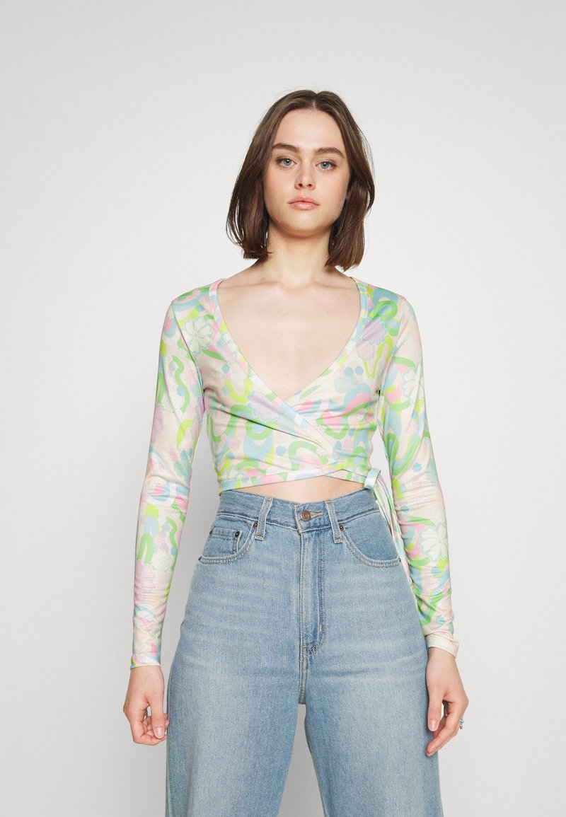 Top cropped de manga longa feito de tecido transparente, apresentando um padrão floral pastel com um design de decote em V profundo. Combinado com jeans de cintura alta.