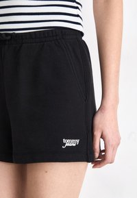 Sorte bomullsshortser med elastisk liv, sidelommer og hvit "tommy jeans" logo. Glatt tekstur, avslappet passform, lengde til midt på låret.