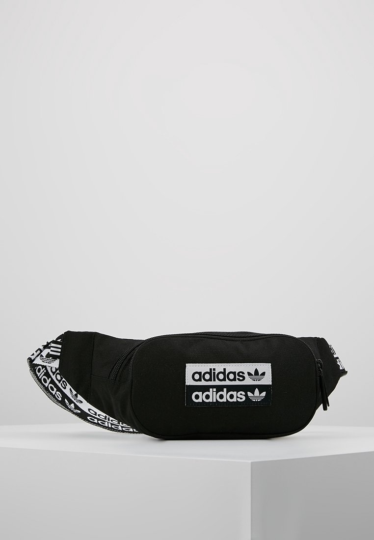Černý plátěný ledvinka se zipem v hlavní přihrádce. Obsahuje bílé nášivky s logem Adidas a nastavovací popruh se značkovým opakovaným textem.