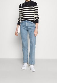 Gestreifter Strickpullover in Marineblau und Creme, hochgeschnittene hellblaue Jeans mit geradem Bein, weiße Sneakers und eine kleine weiße Handtasche.
