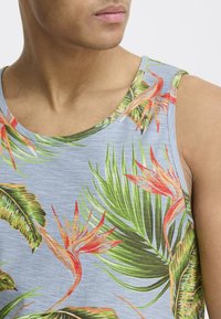 Tropisk mønster tanktop i lyseblå, med grønne palmeblader og rød/oransje fugl av paradis-blomster, laget av myk tekstil.