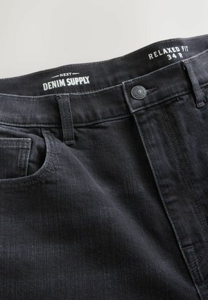 Sorte løstsiddende jeans med knap foran og bæltestropper, mærket "Next Denim Supply" og størrelse "34R" indeni linningen.