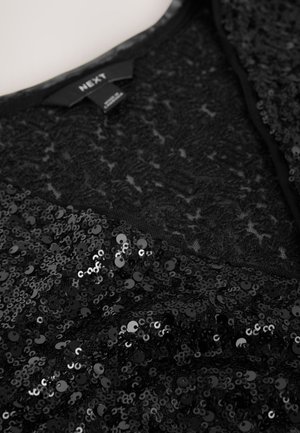 Svart plagg med paljetter, som har spetsstruktur, V-ringning och slät fodring. Paljetterna ger en skimrande effekt som framhäver designdetaljerna.