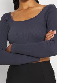 Halenka s dlouhými rukávy, žebrovaná, v námořnické modři, s širokým kulatým výstřihem, s přiléhavým střihem a hladkou texturou. Nosit s černými vysokými kalhotami.
