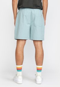 Lichtblauwe shorts met een elastische tailleband en een enkele achterzak. Gekleed met witte sneakers en multi-gekleurde gestreepte sokken.