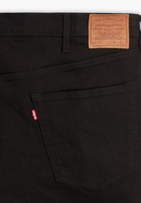 Fekete Levi's farmer zsebén látható piros Levi's címke, a derékpánt felett pedig barna bőrből készült márkajelzés található.