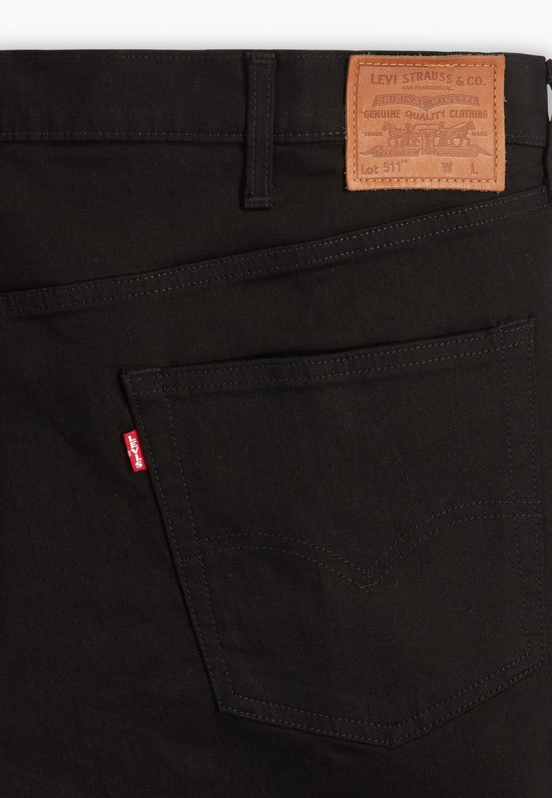 Poche arrière d'un jean Levi's noir avec une étiquette rouge Levi's visible et un patch en cuir marron de la marque au-dessus de la taille.