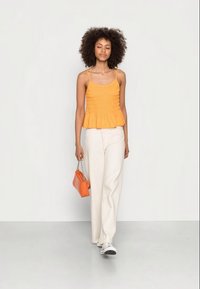 Top peplum laranja com alças spaghetti; tecido texturizado. Combinado com calças largas brancas e uma pequena bolsa laranja. Calçado: ténis brancos.