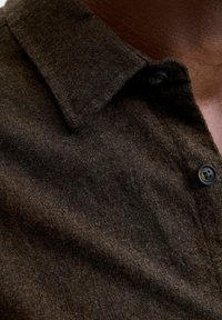 Close-up of dark brown wool shirt collar and upper chest with two black buttons on a person with dark skin.